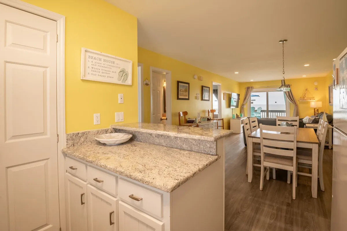 An inviting open-concept living and dining area with yellow walls, a granite countertop, a dining table, and a cozy seating space. The layout offers a glimpse of both relaxation and communal dining, suggesting easy transitions between everyday living and special moments.