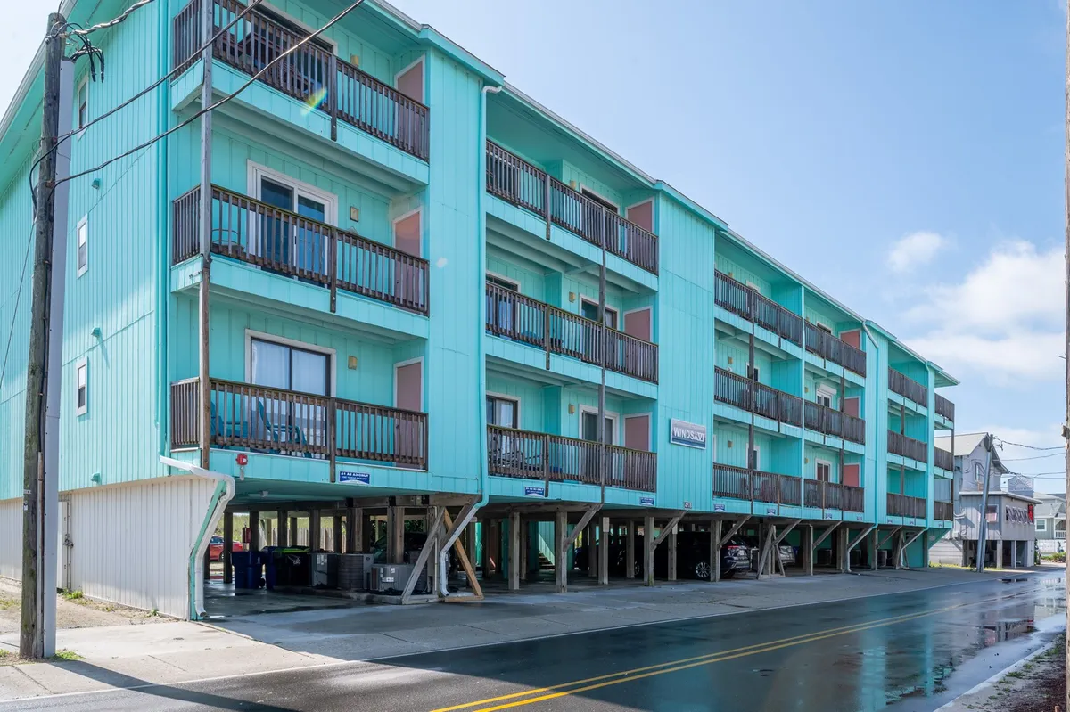 The exterior of the property features a turquoise building with balconies overlooking outdoor spaces. The setting invites guests to relax on the balcony while enjoying the view or the ocean air, reinforcing the sense of a calm, residential environment.