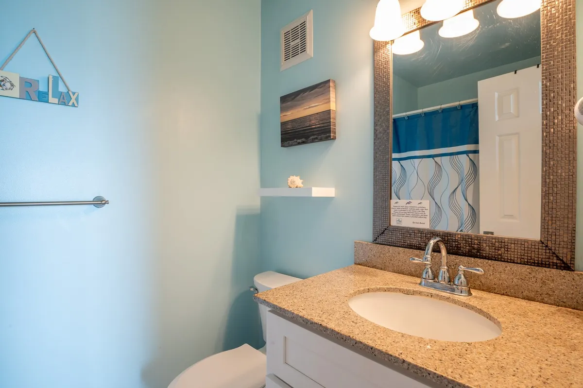 A calming ensuite bathroom featuring a granite countertop, large mirror, colorful shower curtain, and tasteful wall art. The ambiance is one of relaxation and comfort, ideal for personal self-care routines.